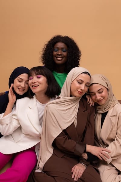 Photo of 5 women seated together looking peaceful. There is one black woman, one east asian woman, and three middle eastern women in hijabs.